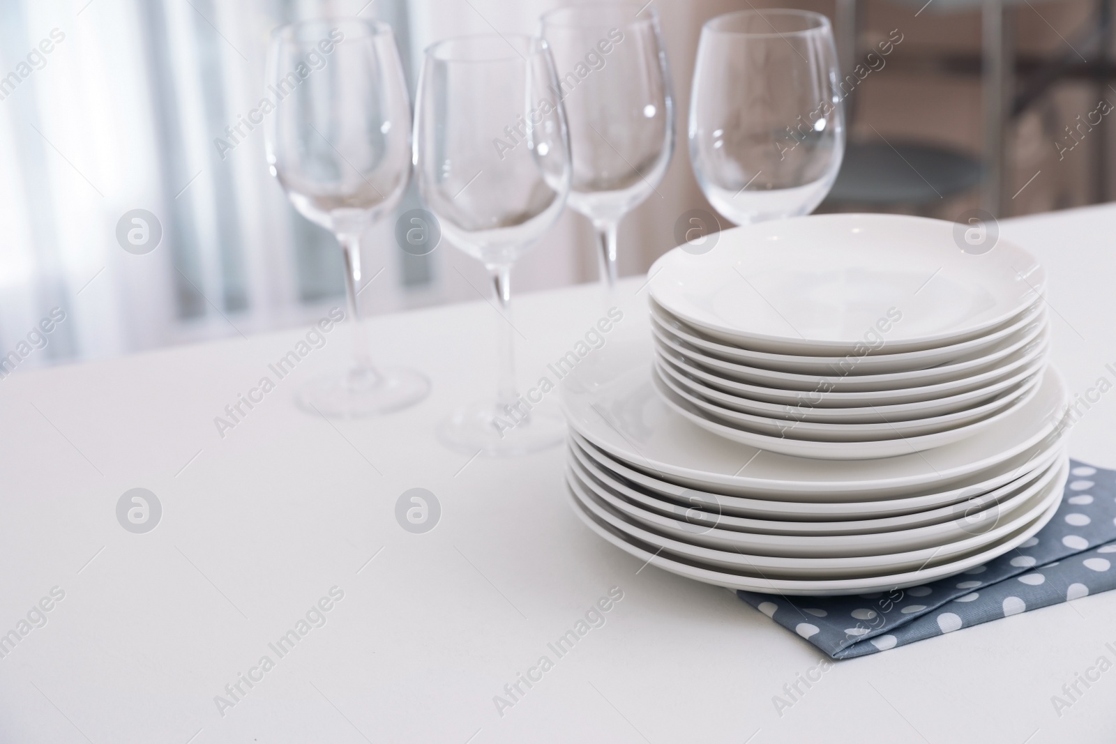 Photo of Stack of clean dishes and glasses on table in kitchen. Space for text