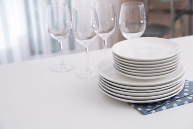 Photo of Stack of clean dishes and glasses on table in kitchen. Space for text