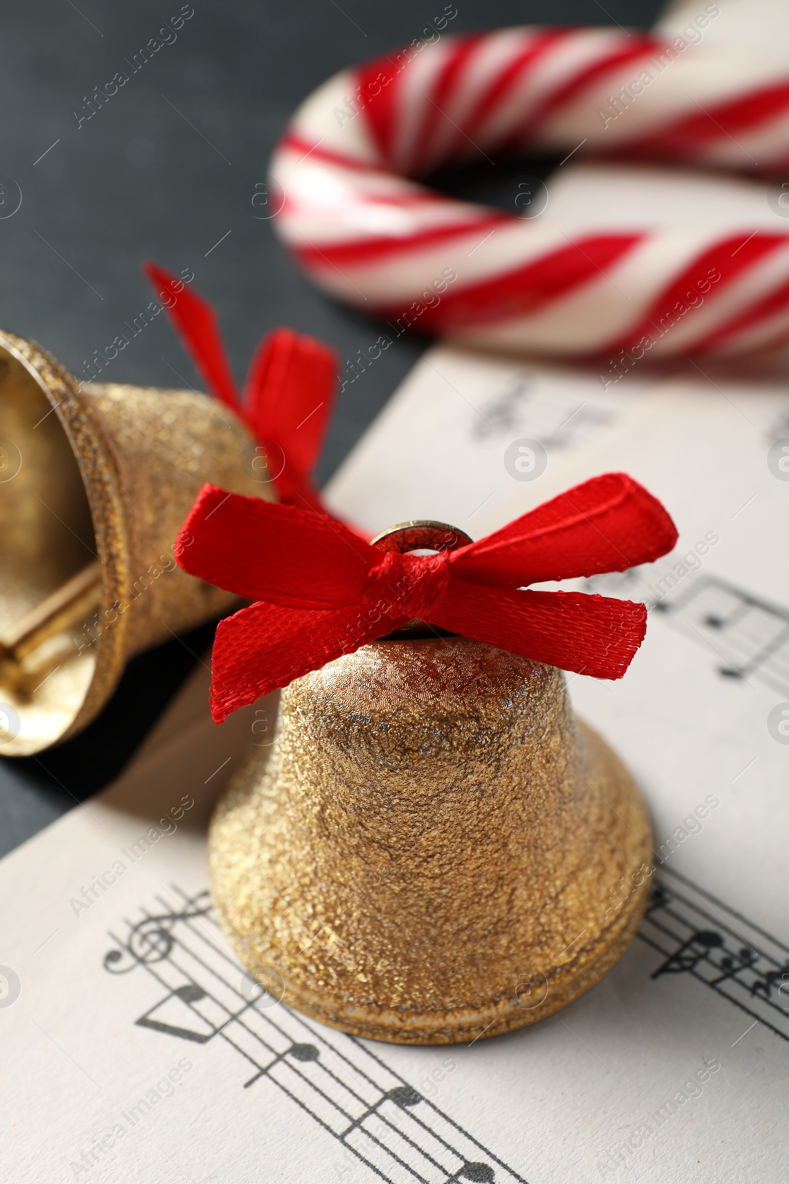 Photo of Golden shiny bells with red bows, music sheets and candy cane on grey table, closeup. Christmas decoration