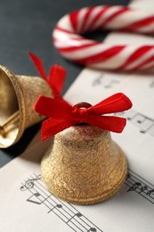 Photo of Golden shiny bells with red bows, music sheets and candy cane on grey table, closeup. Christmas decoration