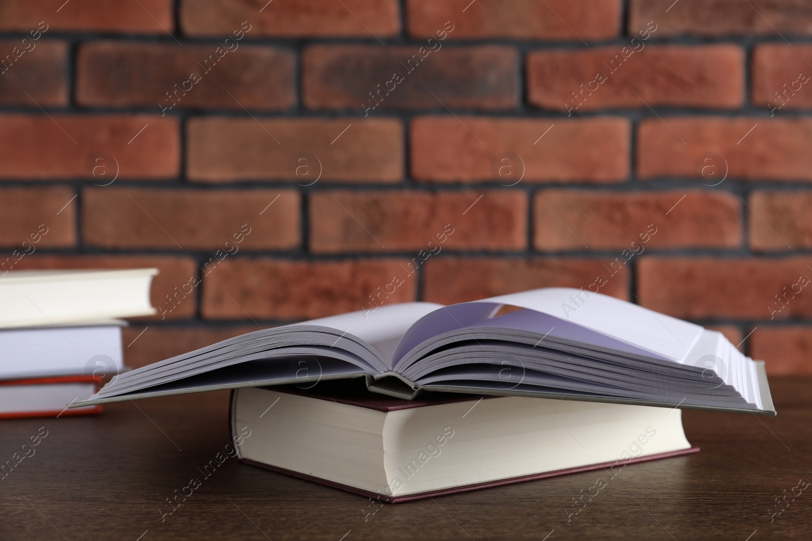 Photo of Hardcover books on wooden table near brick wall