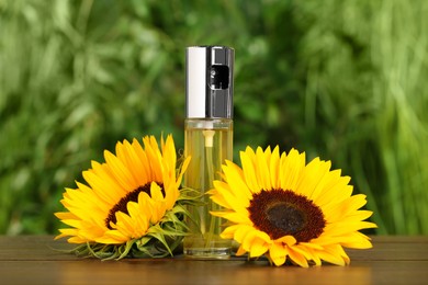 Photo of Sunflowers and spray bottle with cooking oil on wooden table against blurred green background