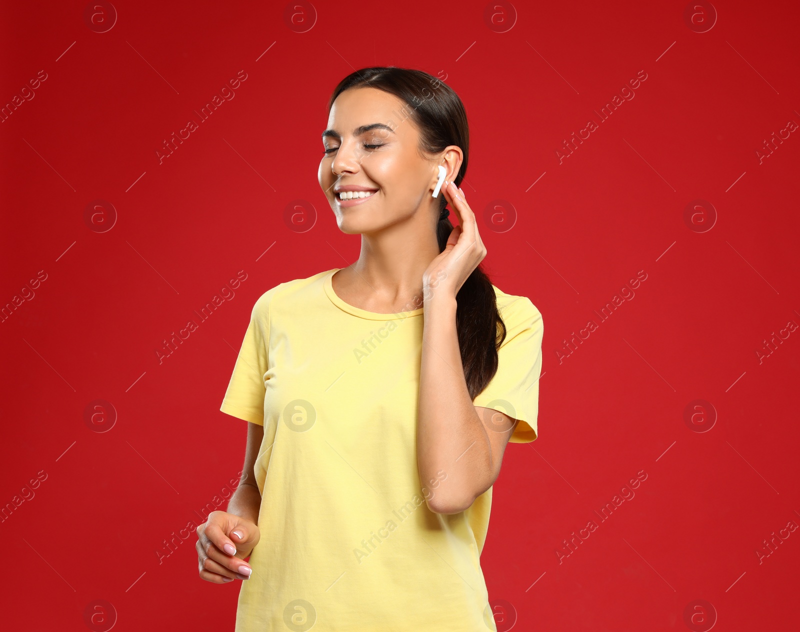 Photo of Happy young woman listening to music through wireless earphones on red background