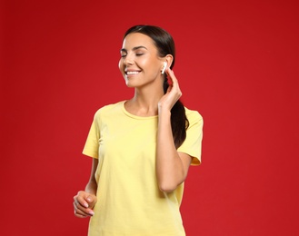 Happy young woman listening to music through wireless earphones on red background