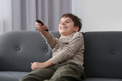 Photo of Happy boy changing TV channels with remote control on sofa at home