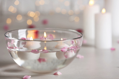 Glass bowl with burning candles and petals on grey stone table