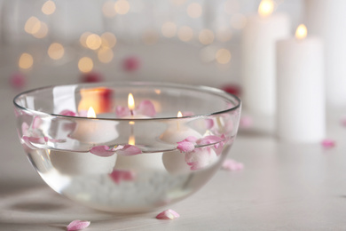 Photo of Glass bowl with burning candles and petals on grey stone table