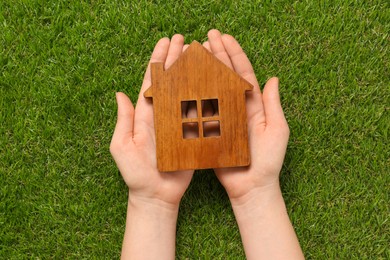 Woman holding house figure on green grass background, top view