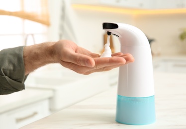 Photo of Man using automatic soap dispenser in kitchen, closeup