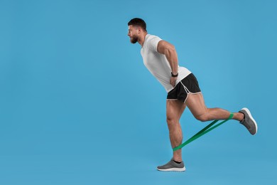 Photo of Young man exercising with elastic resistance band on light blue background. Space for text