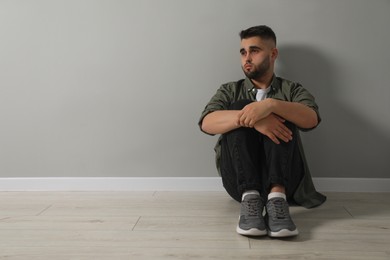 Photo of Sad man sitting on floor near light grey wall. Space for text