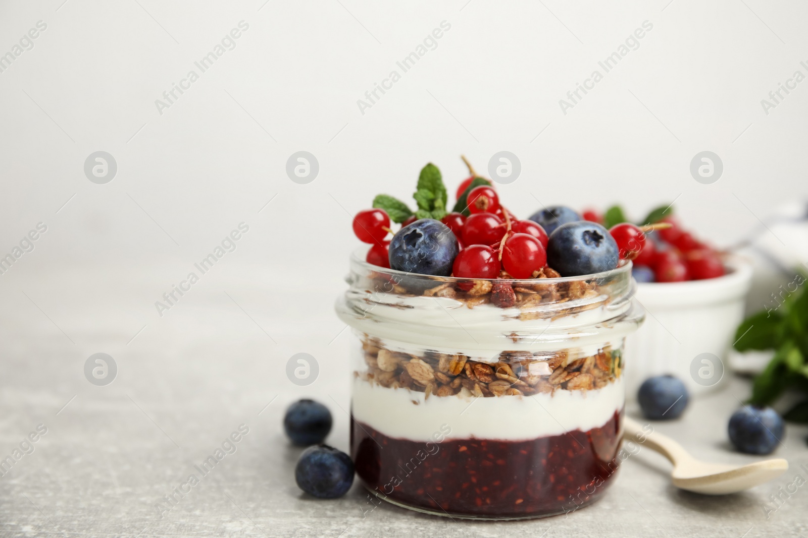 Photo of Delicious yogurt parfait with fresh berries and mint on light grey table, space for text