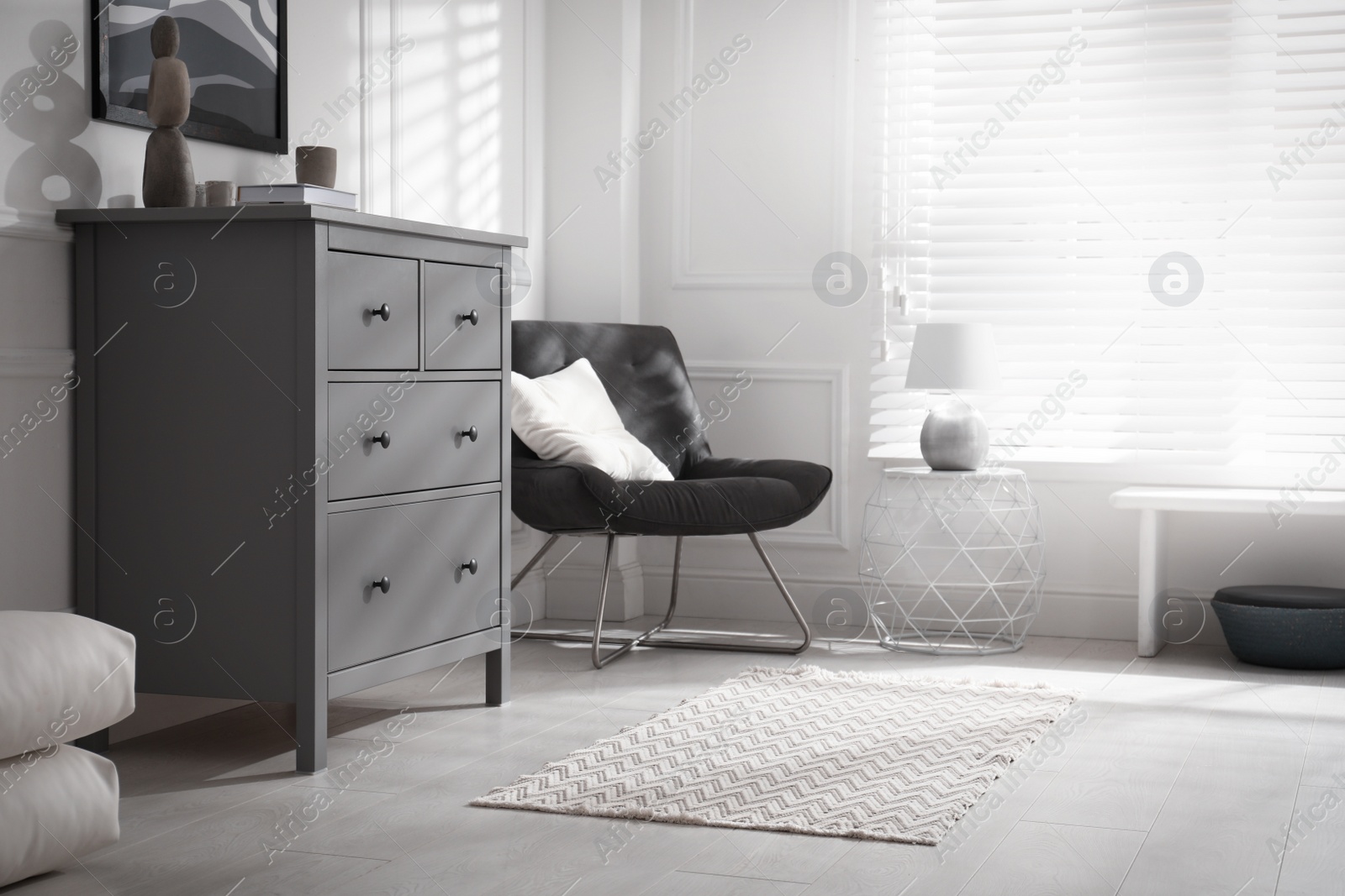 Photo of Stylish room interior with grey chest of drawers and comfortable chair