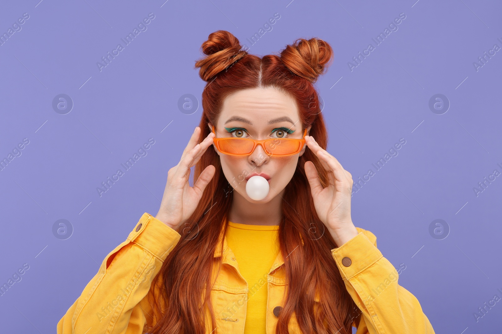 Photo of Portrait of beautiful woman in sunglasses blowing bubble gum on violet background