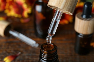 Photo of Dripping essential oil from pipette into bottle on wooden table, closeup