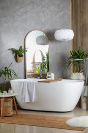 Modern white tub and beautiful green houseplants in bathroom. Interior design