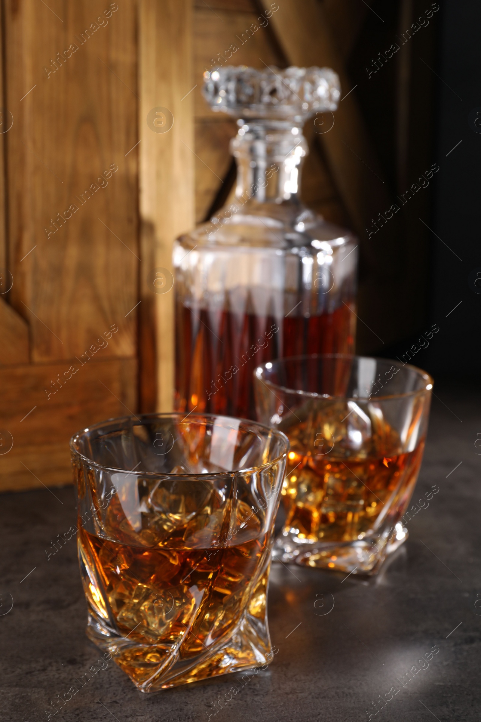 Photo of Whiskey with ice cubes in glasses and bottle on grey table