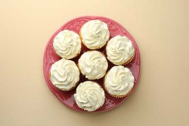 Tasty vanilla cupcakes with cream on beige background, top view