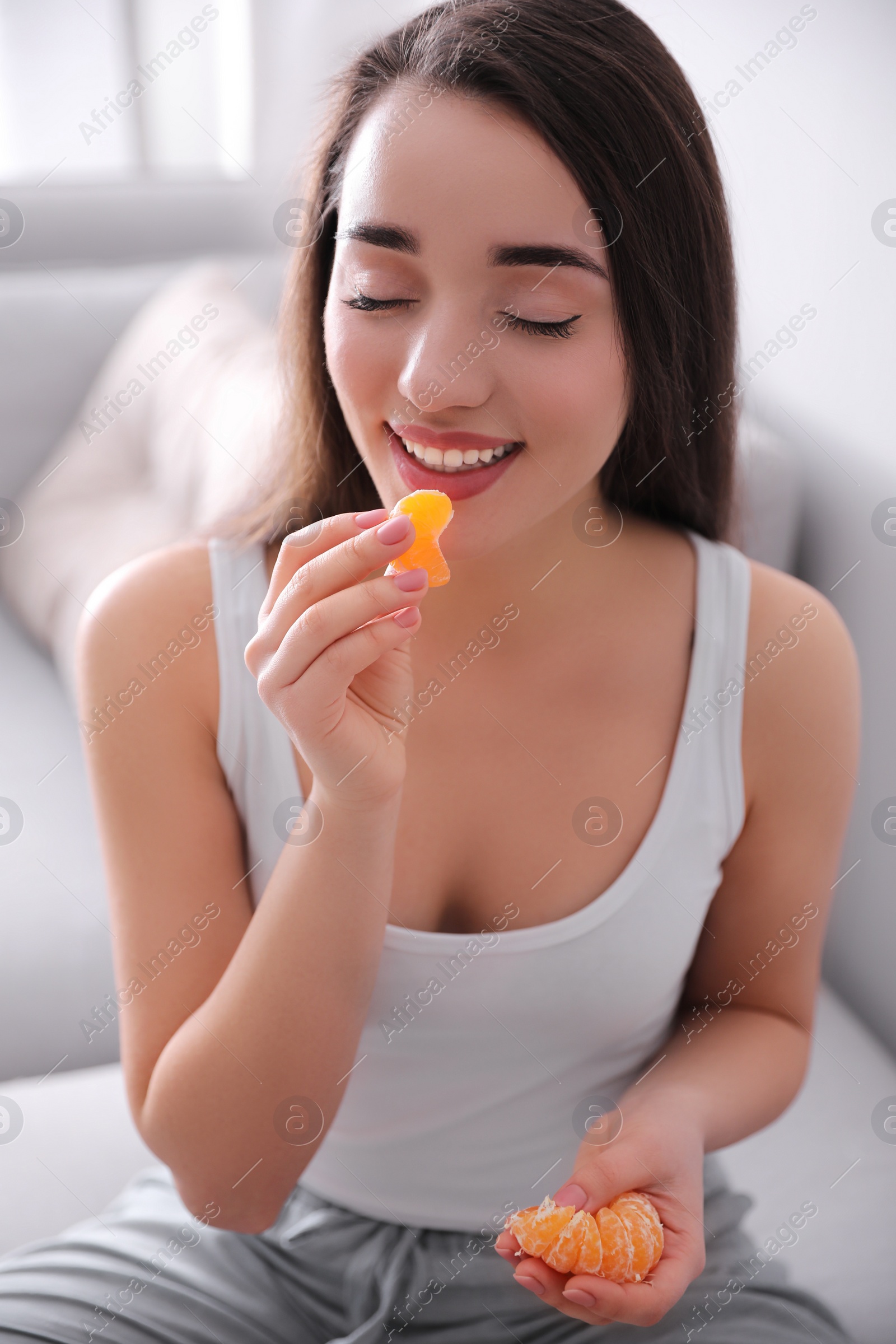 Photo of Happy young woman eating ripe tangerine at home