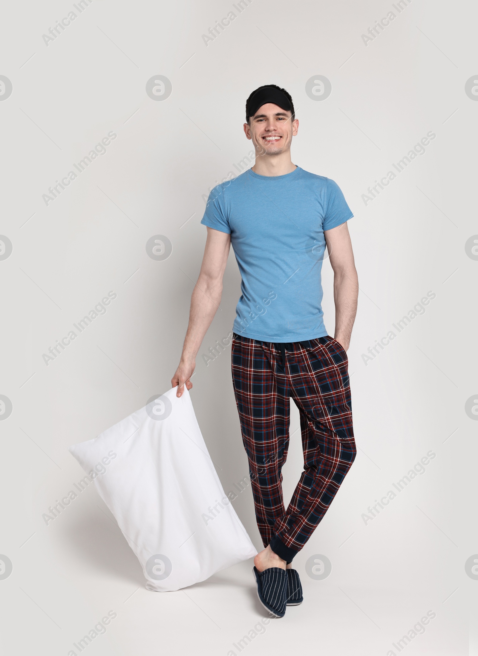 Photo of Happy man in pyjama and sleep mask holding pillow on light grey background