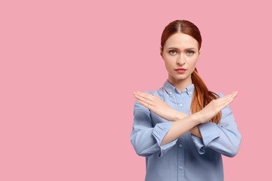 Photo of Stop gesture. Woman with crossed hands on pink background, space for text