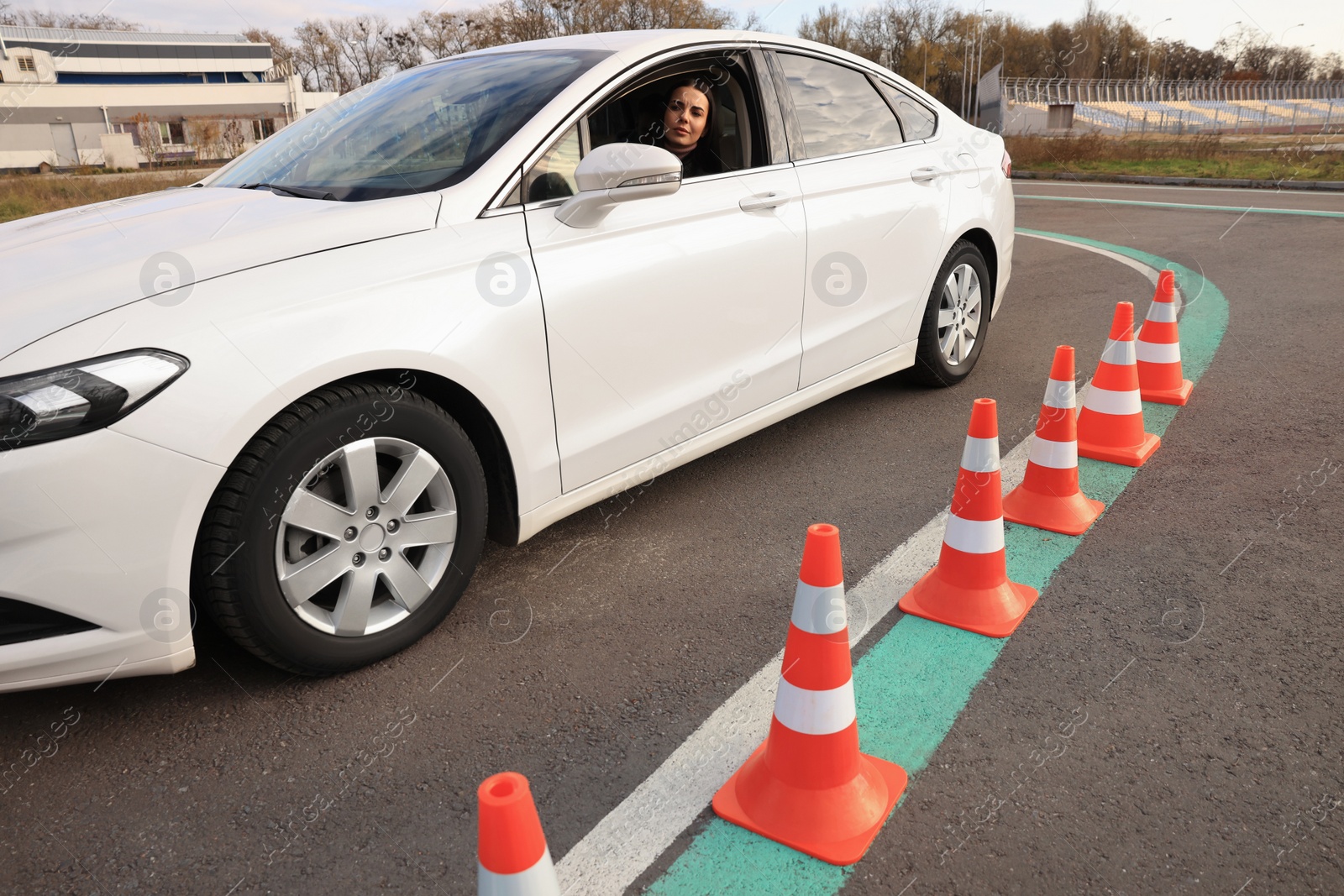 Photo of Young woman in car on test track with traffic cones. Driving school