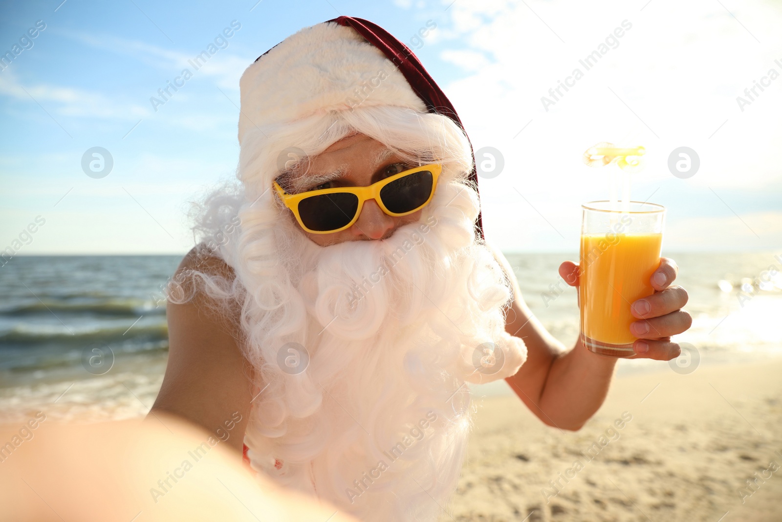 Photo of Santa Claus with cocktail taking selfie on beach. Christmas vacation