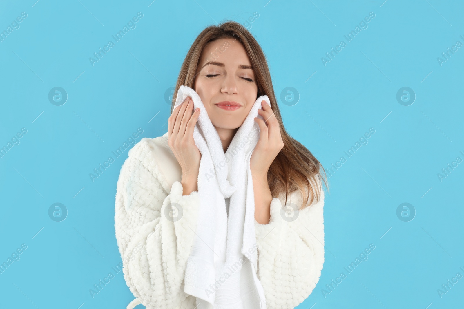 Photo of Young woman wiping face with towel on light blue background