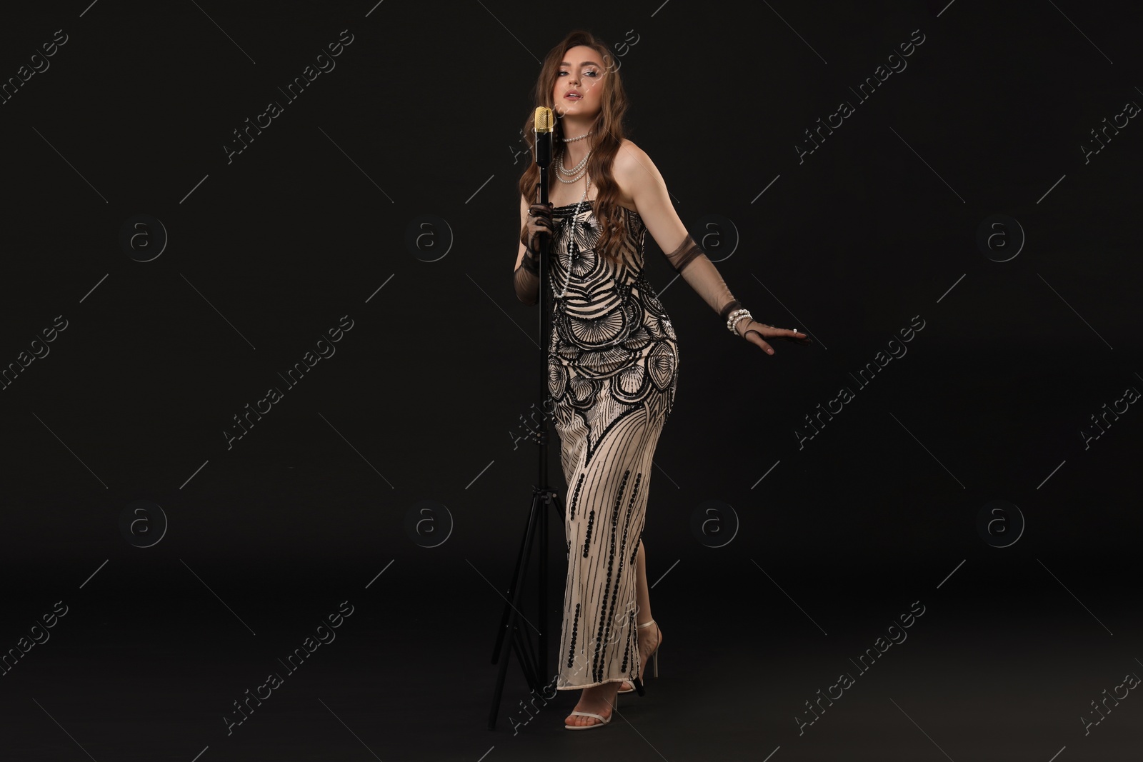 Photo of Beautiful young woman in stylish dress with microphone singing on black background