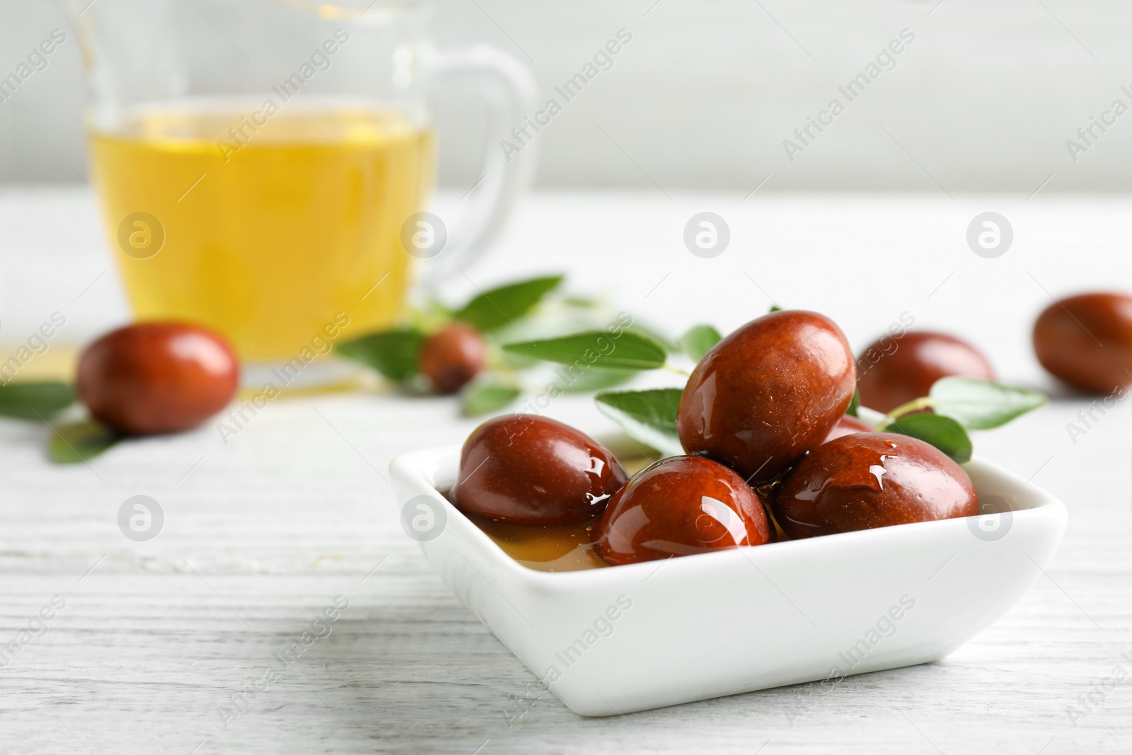 Photo of Sauce boat with jojoba oil and seeds on white wooden table