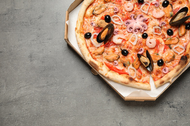 Photo of Delicious seafood pizza in box on grey table, top view. Space for text