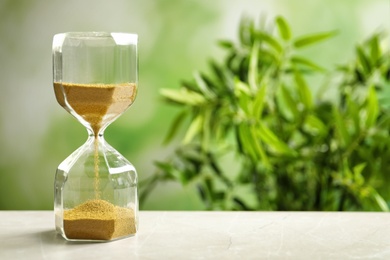 Photo of Hourglass with flowing sand on table against blurred background. Time management