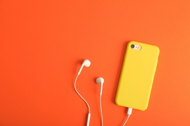 Photo of Modern phone with earphones on coral background, top view. Space for text