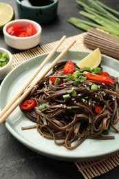 Photo of Tasty buckwheat noodles (soba) with chili pepper, onion and chopsticks on grey table, closeup