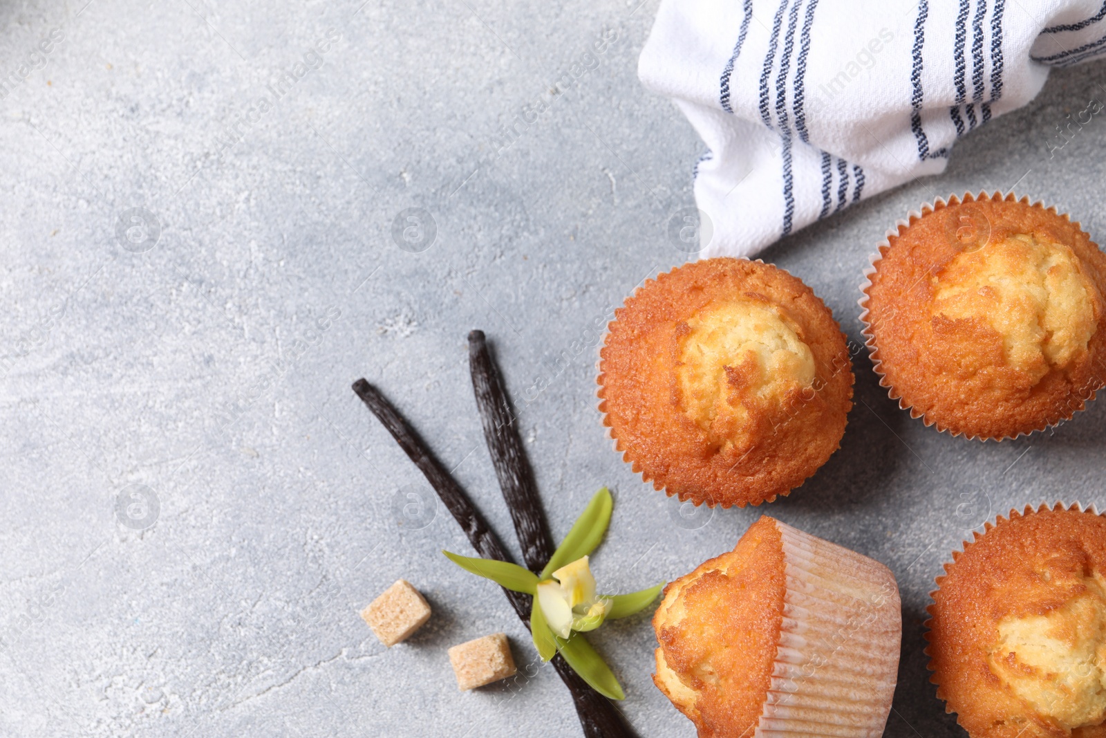 Photo of Delicious sweet muffins, vanilla pods and brown sugar on light grey textured table, flat lay. Space for text