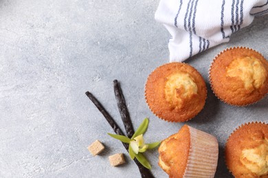 Delicious sweet muffins, vanilla pods and brown sugar on light grey textured table, flat lay. Space for text