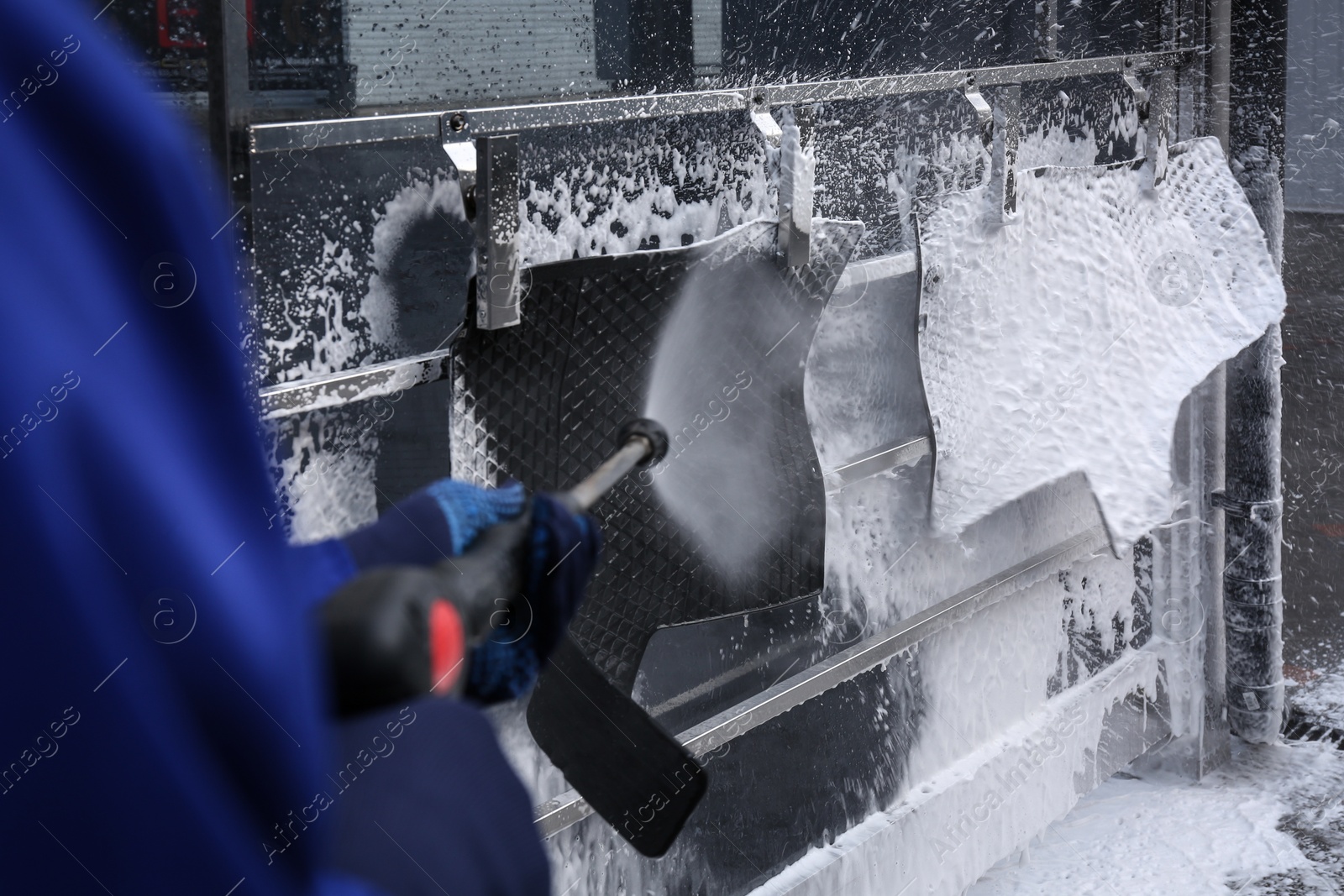 Photo of Worker cleaning automobile floor mats with high pressure water jet at car wash, closeup