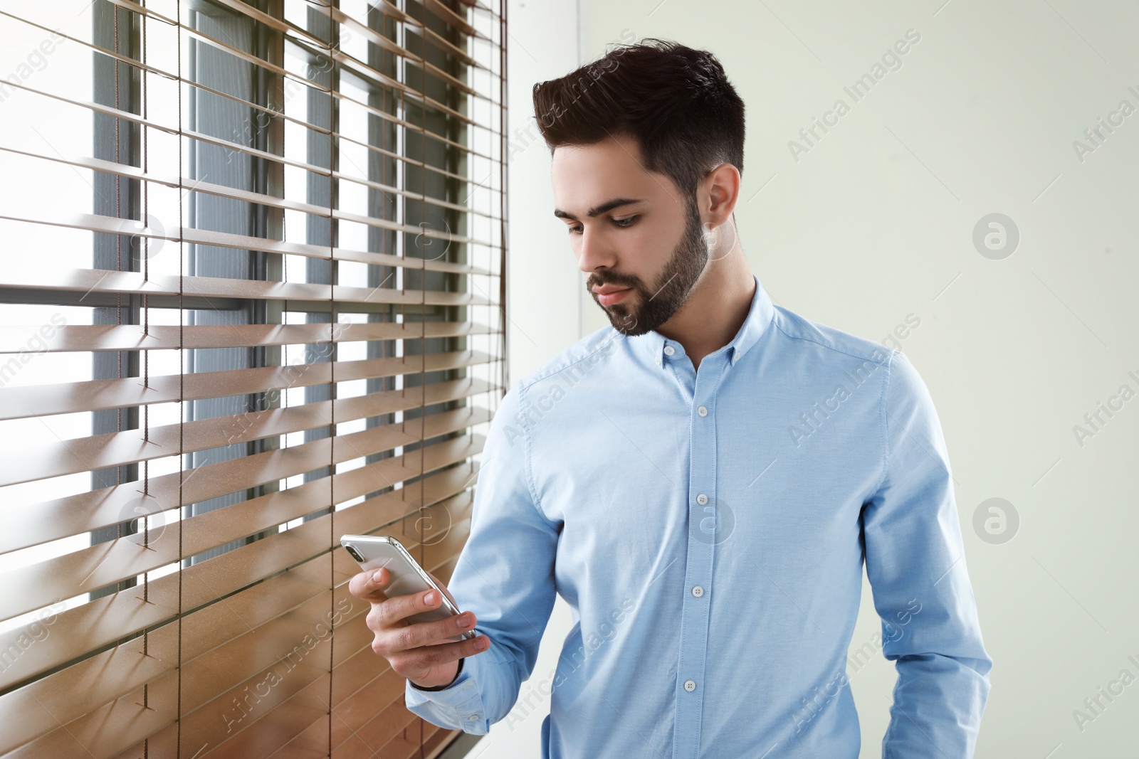 Photo of Handsome man with mobile phone at window indoors