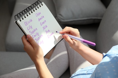 Pregnant woman with baby names list sitting on sofa, closeup