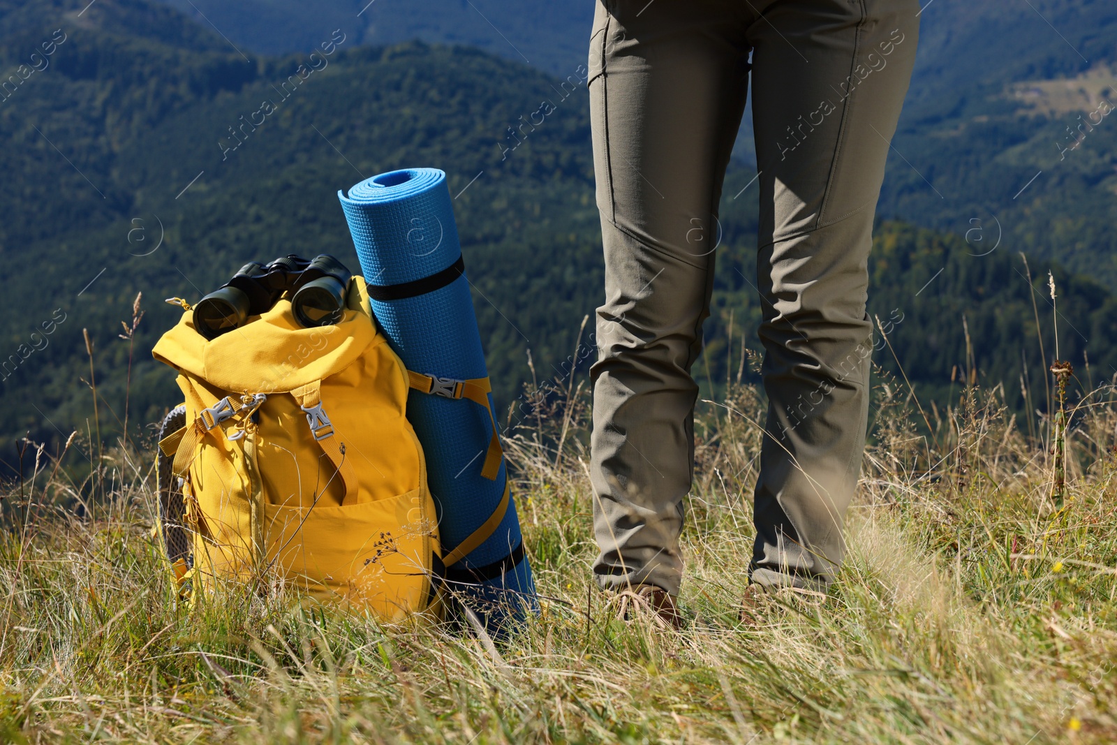 Photo of Tourist with backpack, sleeping pad and binoculars in mountains on sunny day, closeup