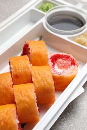 Photo of Delicious mamenori sushi rolls in plastic container on table, closeup. Food delivery