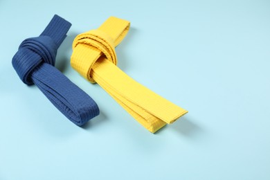 Photo of Colorful karate belts on light blue background, space for text