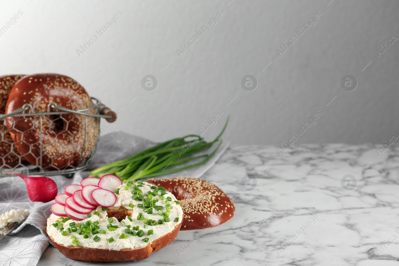 Photo of Delicious bagel with cream cheese, radish and green onion on white marble table. Space for text