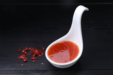 Photo of Chili sauce in spoon on black wooden table, closeup. Space for text