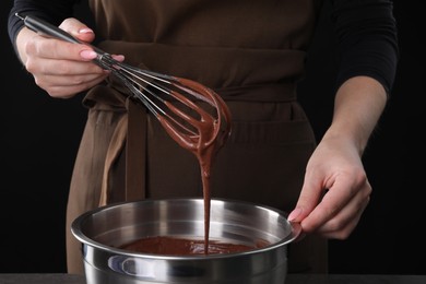 Photo of Woman with whisk mixing chocolate cream on black background, closeup