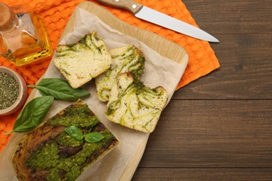 Photo of Freshly baked pesto bread with basil served on wooden table, flat lay. Space for text