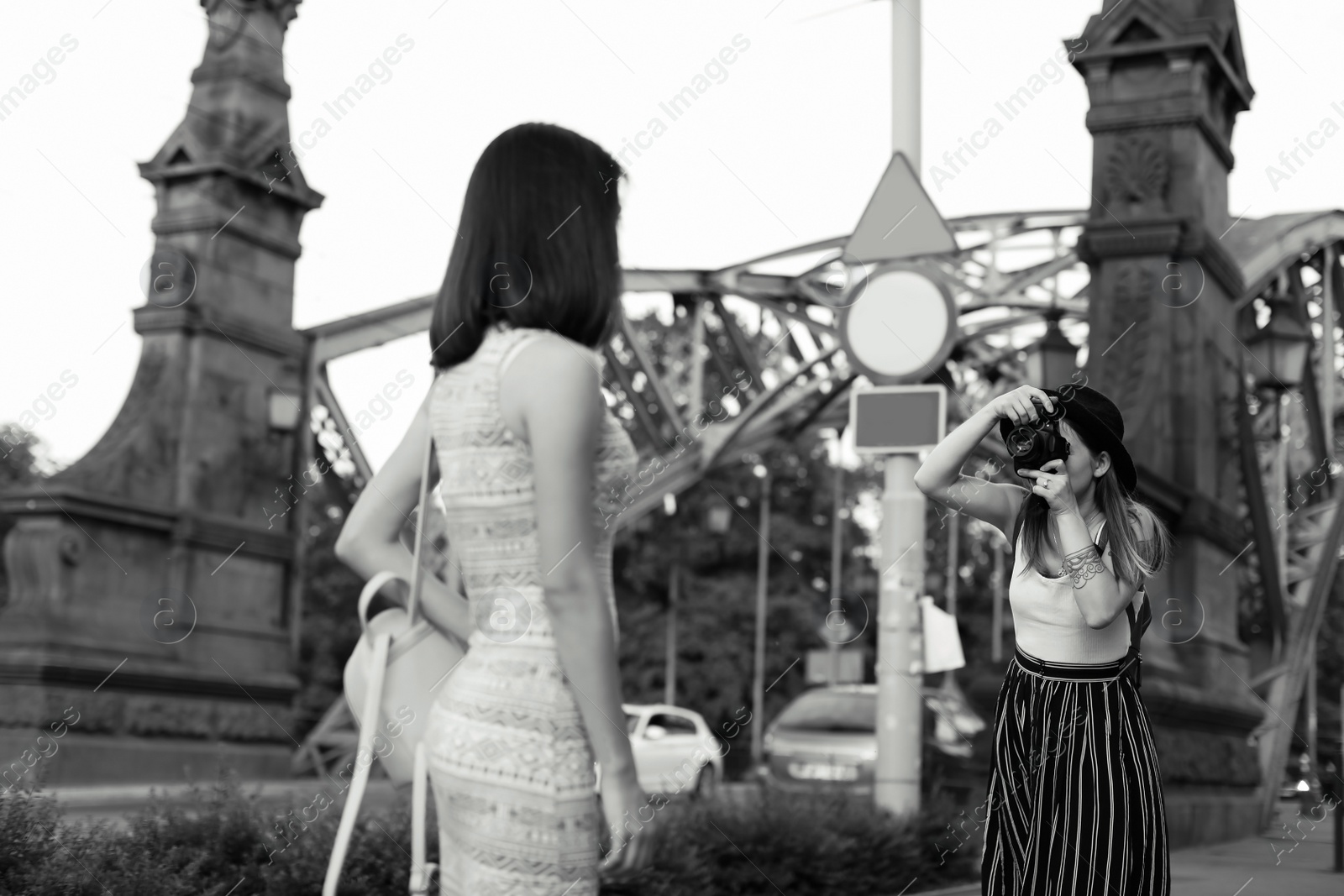 Photo of Young woman taking photo of her friend on city street, black and white effect
