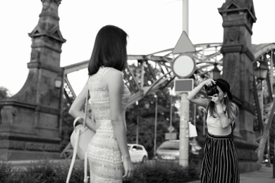 Young woman taking photo of her friend on city street, black and white effect