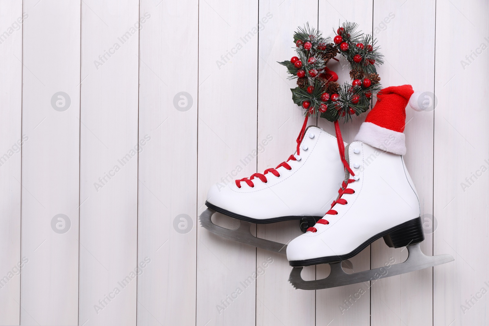 Photo of Pair of ice skates and Christmas wreath hanging on white wooden background, space for text