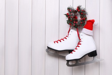 Pair of ice skates and Christmas wreath hanging on white wooden background, space for text